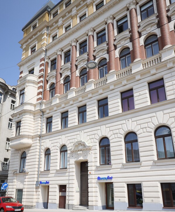 Un edificio de varios pisos con arquitectura clásica, que destaca por su entrada en esquina, ventanas amplias y una señal de calle visible.