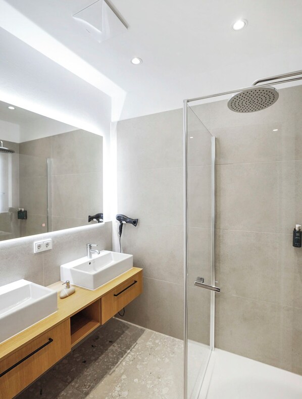 Un baño moderno con dos lavamanos, ducha y un espejo grande.