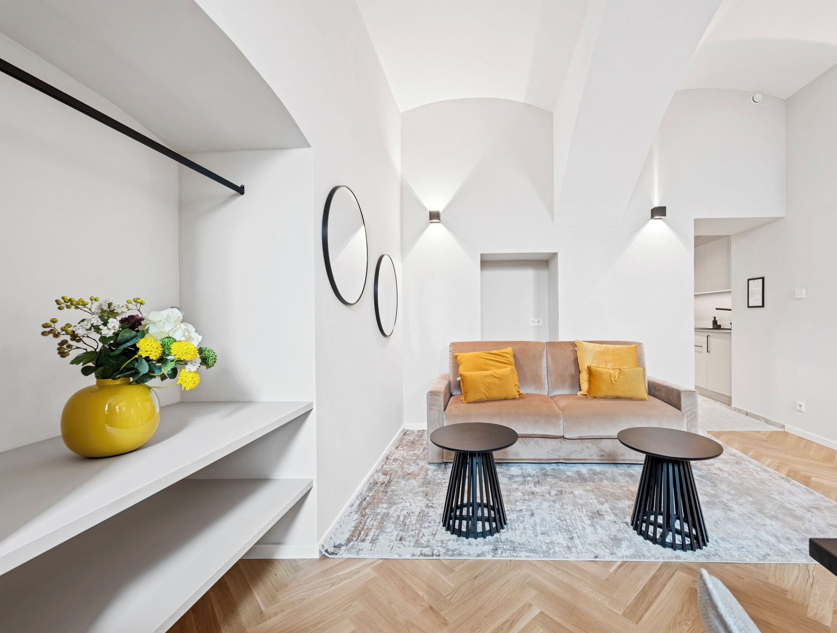 Un apartamento moderno con un conjunto de sofás, dos mesas auxiliares y un jarrón amarillo con flores.
