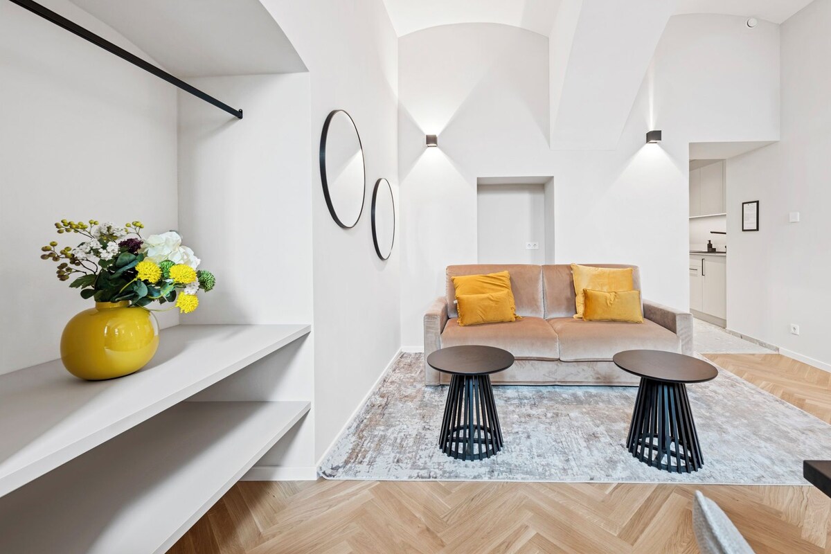 A modern apartment with a sofa set, two side tables, and a yellow vase with flowers.