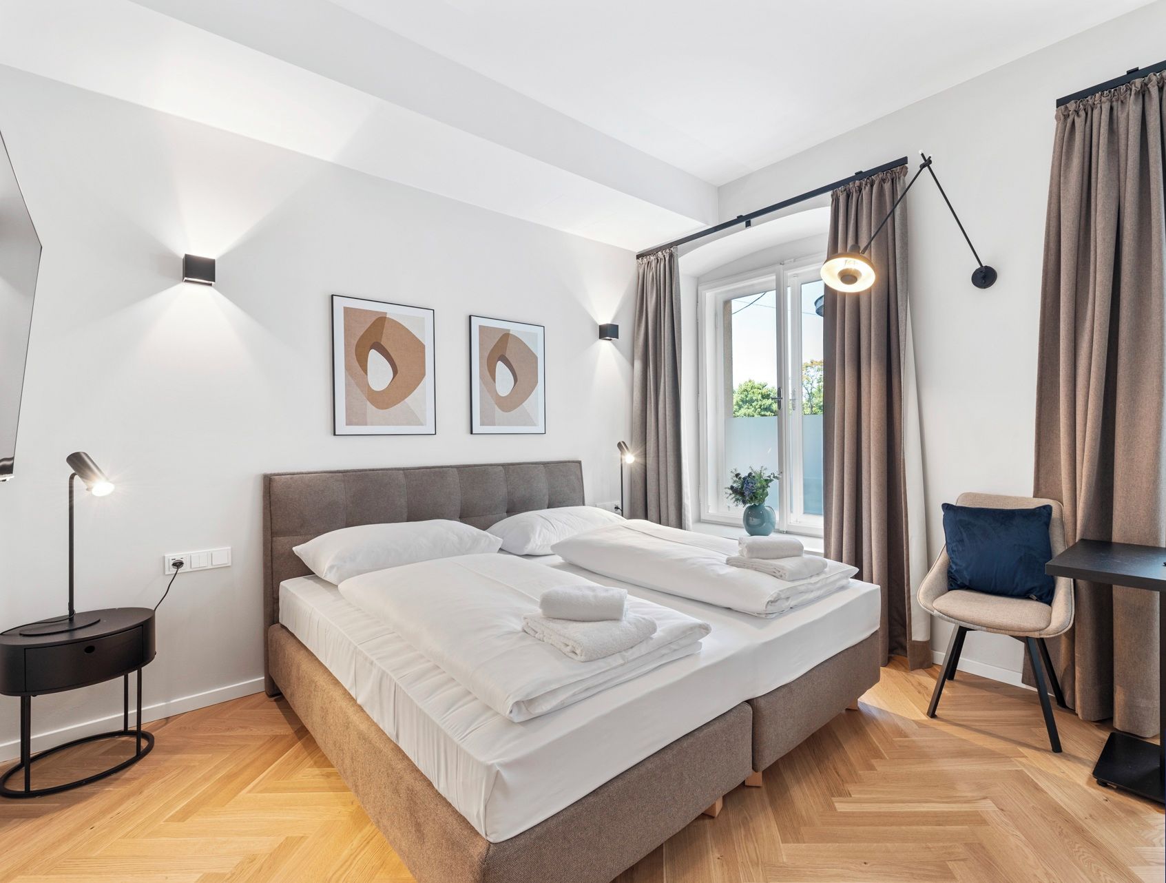 Un dormitorio moderno con una cama doble, lámparas de noche, un escritorio con una silla y una ventana con cortinas.