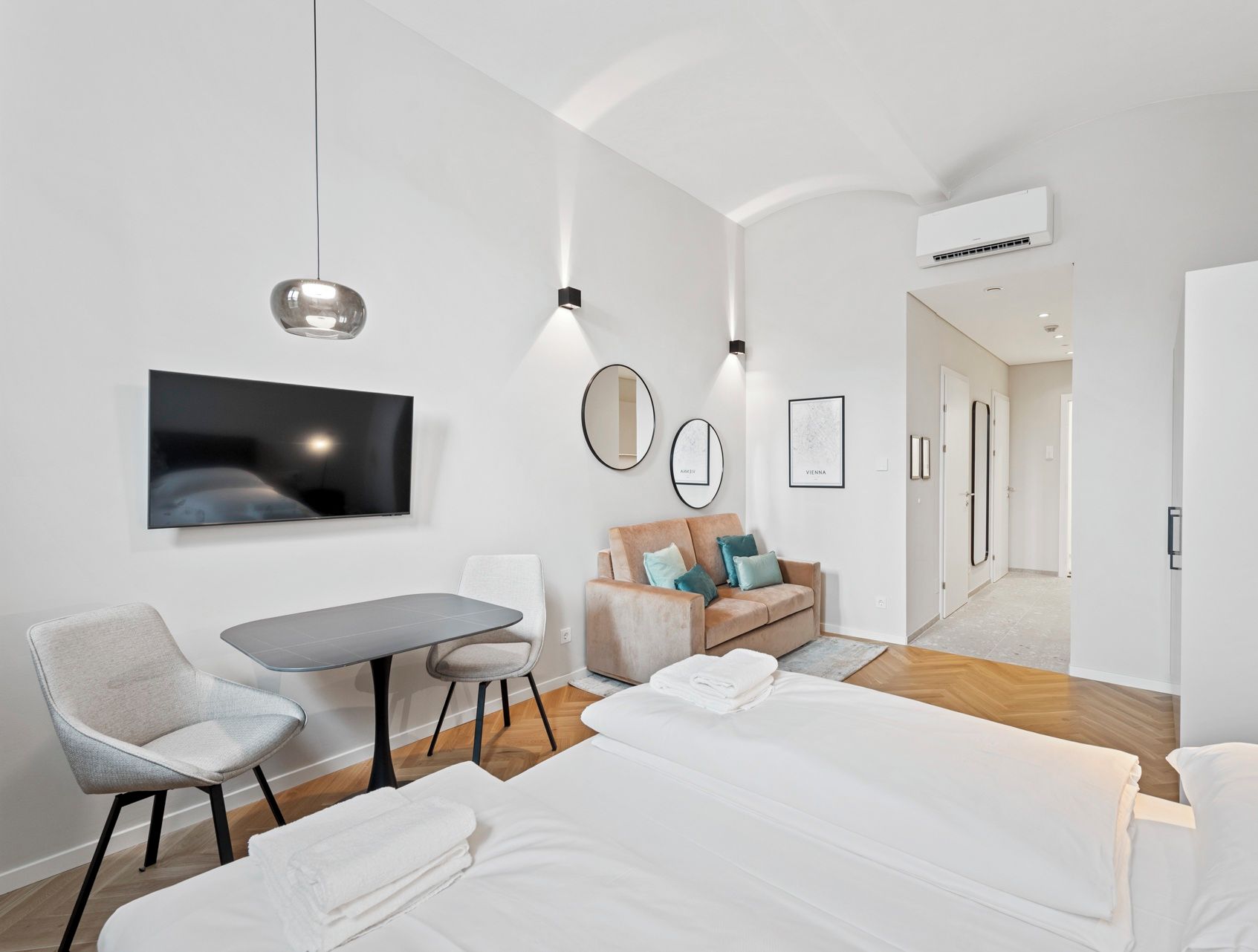 A modern hotel room with a bed, a desk, a chair, a sofa, a TV, and a mirror.