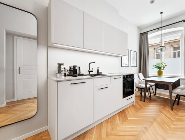 A compact one-bedroom apartment with a kitchenette, a dining area, and a window with curtains. - easy-flat Stadtpark - Premium AC Apartments (Vienna)
