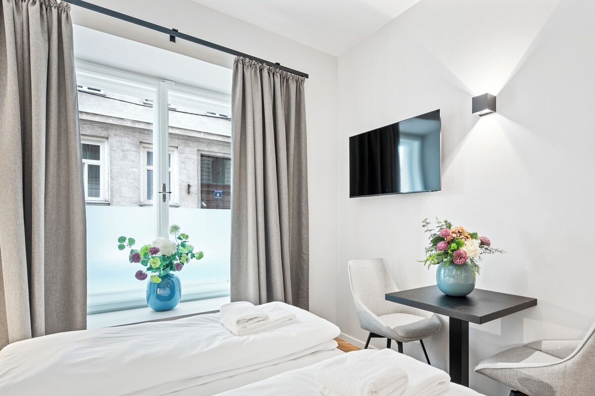 A hotel room with a bed, a desk, a chair, a TV, and a window with curtains.