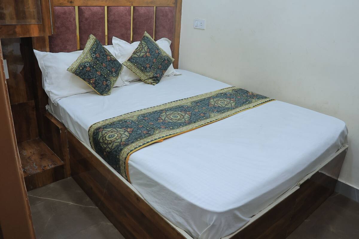 A single bed with a white mattress, two decorative pillows, and a patterned bedspread.