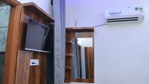Una habitación con un armario de madera, televisor, espejo y aire acondicionado instalado en la pared.