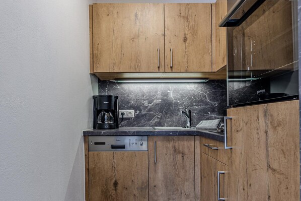 A compact kitchen with wooden cabinets, a built-in coffee maker, and a marble backsplash. - Nice apartment in Jochberg with ski-in, out (Jochberg)