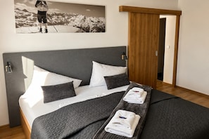 Una cama bien hecha con un edred ón gris, almohadas blancas y una toalla doblada.