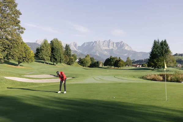 A golf course with a clear view of mountains in the background, a well-maintained green, and a flagstick.