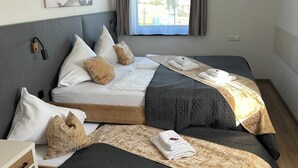 A double bed with a grey quilted cover, white pillows, and a beige throw blanket. There is a small bedside table with a drawer and a lamp. - Apartment in Jochberg with ski-in/out (Jochberg)