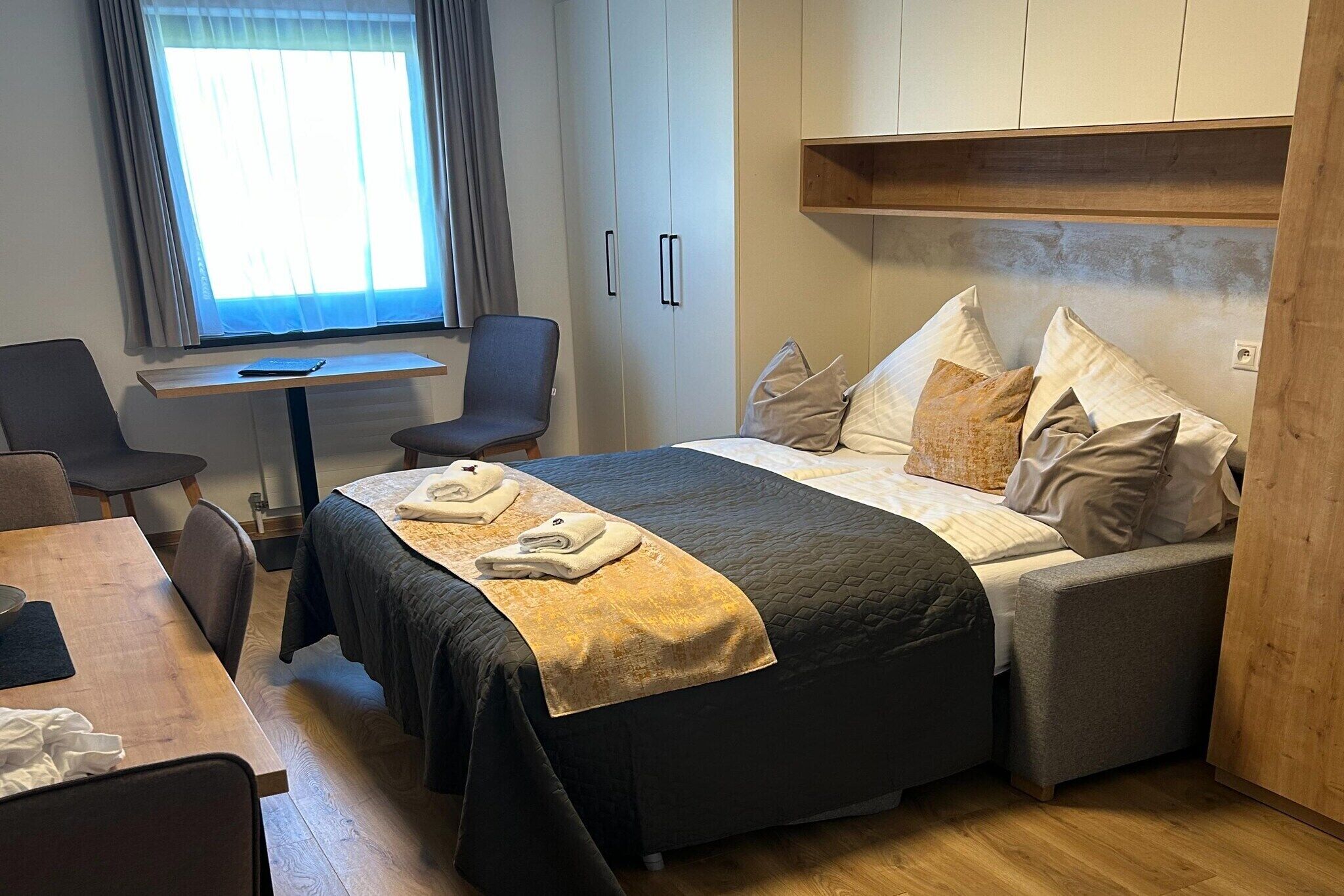 A neatly arranged hotel room with a bed, a desk, and a chair.