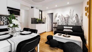 A modern kitchen with white cabinets, a dining table set for four, and a black and white patterned wall mural. - Spacious Apartment 2BR/5P – Nogent-sur-Marne (Nogent-sur-Marne)
