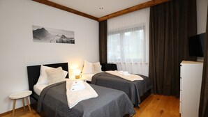 Et hotelværelse med to senge, et lille bord, et fjernsyn og et billede på væggen.