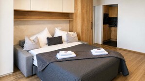 Et moderne hotelværelse med seng, grå sofa, træpanelfag og et tekøkken.