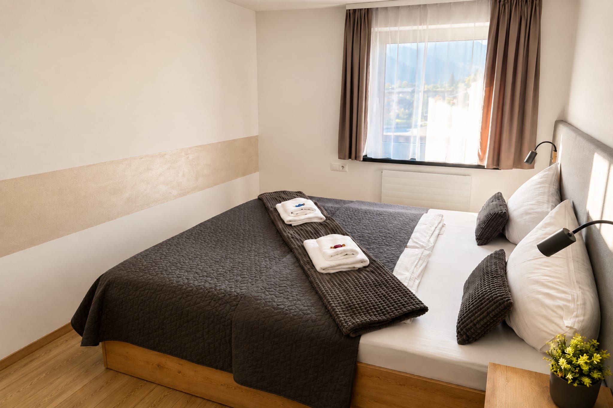 Een hotelkamer met een bed, een raam met gordijnen, een bedlampje en een kleine plant op het nachtkastje.