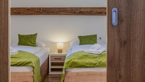Une petite chambre agréable avec deux lits simples, chacun recouvert d’une couverture et d’un oreiller verts. Une table de chevet avec une lampe se trouve entre les deux lits.