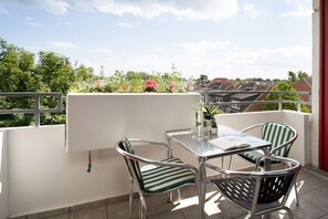 A balcony with a table and chairs, a potted plant, and a view of buildings and greenery. - Berolina 314 - Sea whispers - "Sea whispers" with a view of the infinite (Dahme)