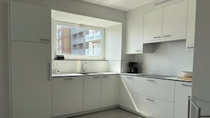 Une cuisine moderne avec des meubles blancs, une fenêtre donnant sur des immeubles et une machine à café.