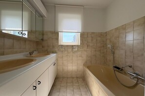 A bathroom with two sinks, a bathtub, and a window with blinds.