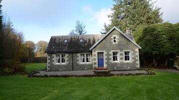 A stone house with a blue door, surrounded by a well-maintained lawn and trees.