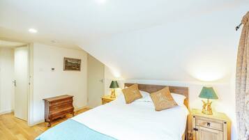 A bedroom with a large bed, two bedside tables with lamps, a wooden dresser, and a painting on the wall.