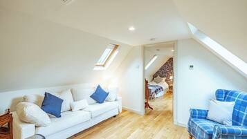 A spacious loft bedroom with a high ceiling, skylights, a wooden floor, a white sofa, a blue plaid sofa, and a bed with floral wallpaper.