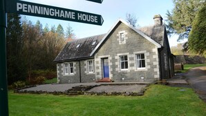A stone house with a blue door, labeled "PENNINGHAM HOUSE," surrounded by a well-maintained lawn and trees.