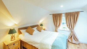 A bedroom with a wooden bed, two bedside lamps, and a window with curtains.