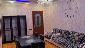 A dining area with a wooden table and chairs, a chandelier, and a patterned sofa. - Sabir bir (Baku)