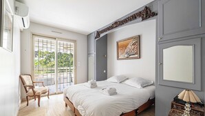 A bedroom with a bed, a chair, a table with a lamp, a painting, and a door. - Apt with A/C and balcony - 1bdr/4P - Cannes/ beach (Cannes)