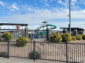 A fenced water park with a green slide and a red structure.