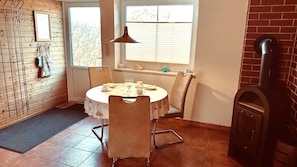 Un coin repas avec une table ronde, des chaises, une fenêtre avec des stores, un luminaire suspendu et un mur en briques.