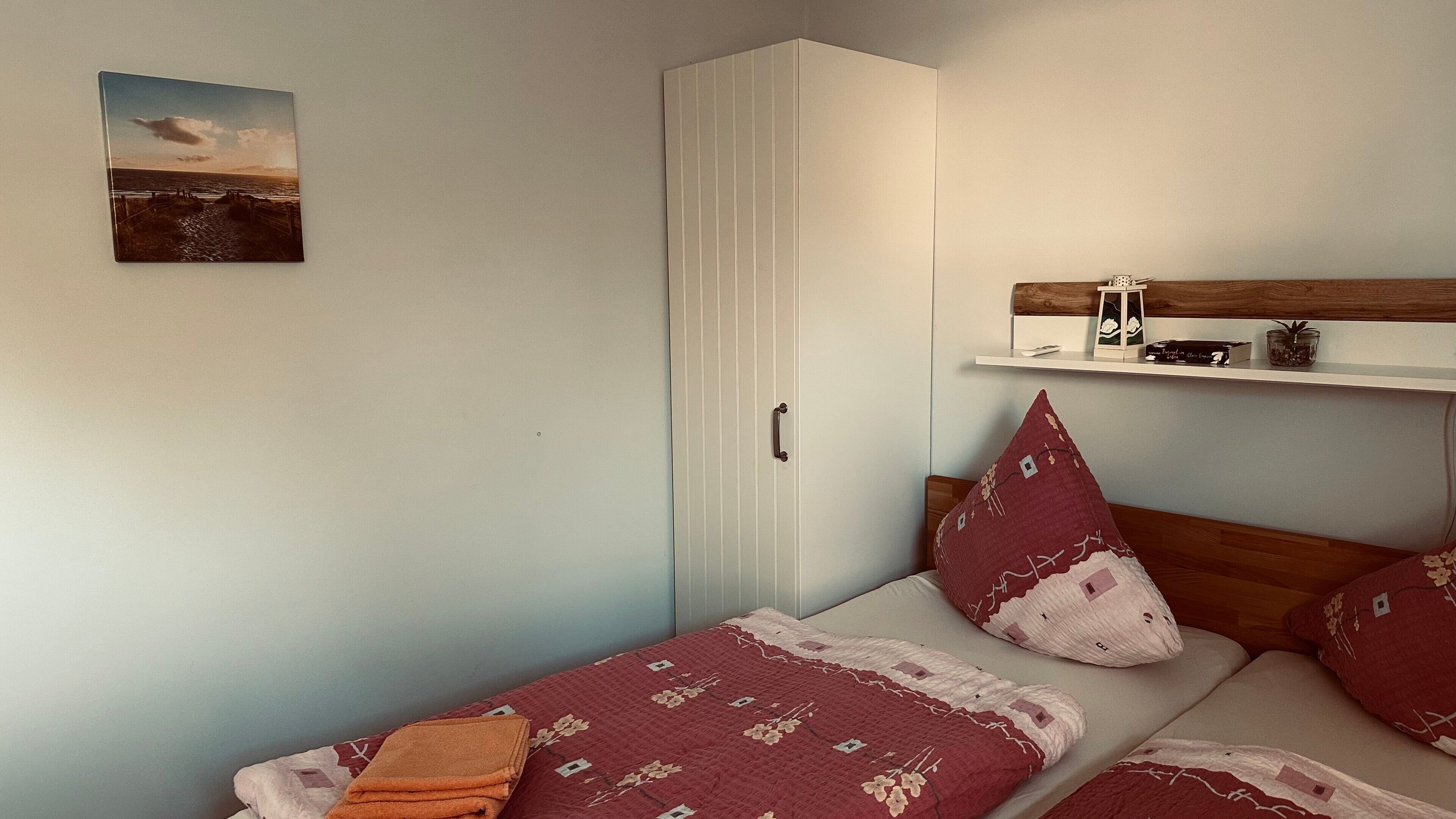 A bedroom with a bed, a wardrobe, a shelf with decorative items, and a painting on the wall.