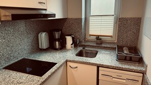 Una cocina compacta con estufa integrada, cafetera, hervidor, lavabo y escurreplatos.