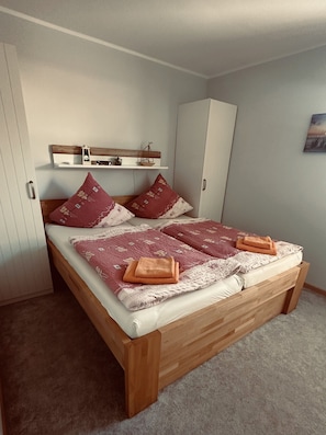Un lit avec un cadre en bois, deux oreillers, une couette et une serviette pliée.