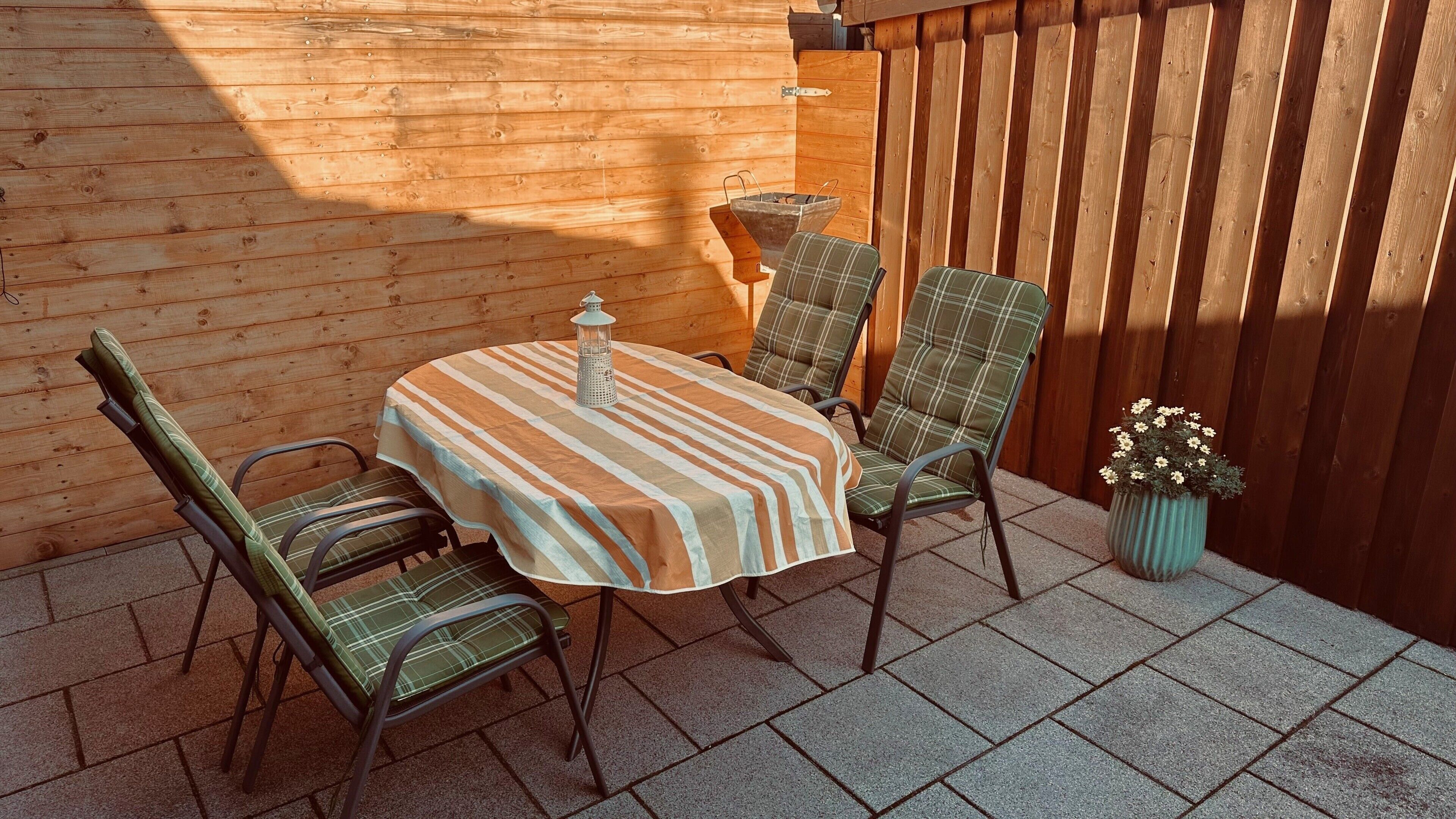 A patio with a round table, two chairs, a lantern, and a potted plant.