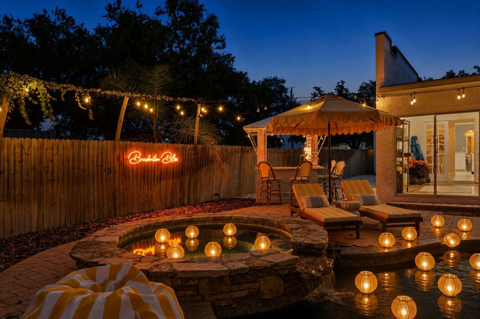 A backyard with a pool, lounge chairs, a wooden fence, and string lights.