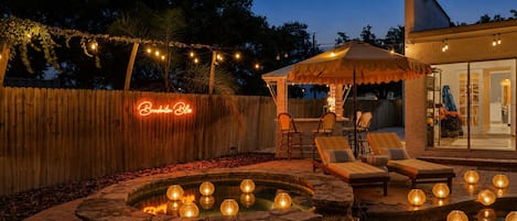 A backyard with a pool, lounge chairs, a wooden fence, and string lights.