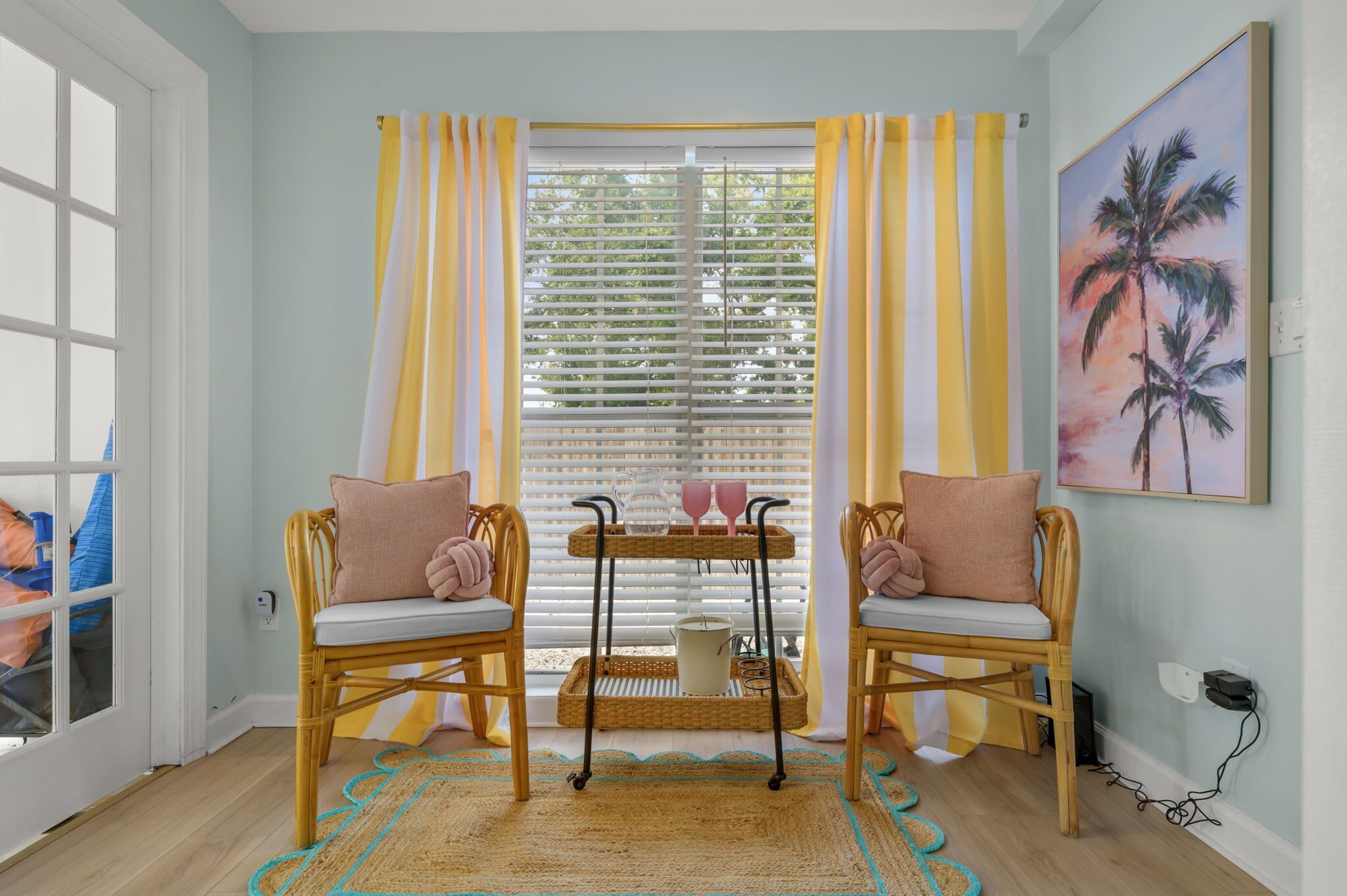 A room with two wicker chairs, a small table, and a window with yellow and white curtains.