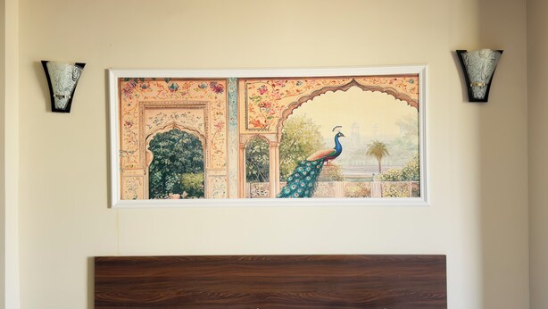 A bed with white bedding and two pillows, one with a floral design, in a room with a wooden headboard and a framed painting of a peacock above the bed. - The Kari INN (Udaipur)