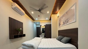 A modern bedroom with a large bed, wooden headboard, and a ceiling fan. - The Kari INN (Udaipur)