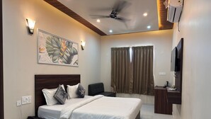A modern hotel room with a large bed, a ceiling fan, a flat-screen TV, and a painting on the wall. - The Kari INN (Udaipur)