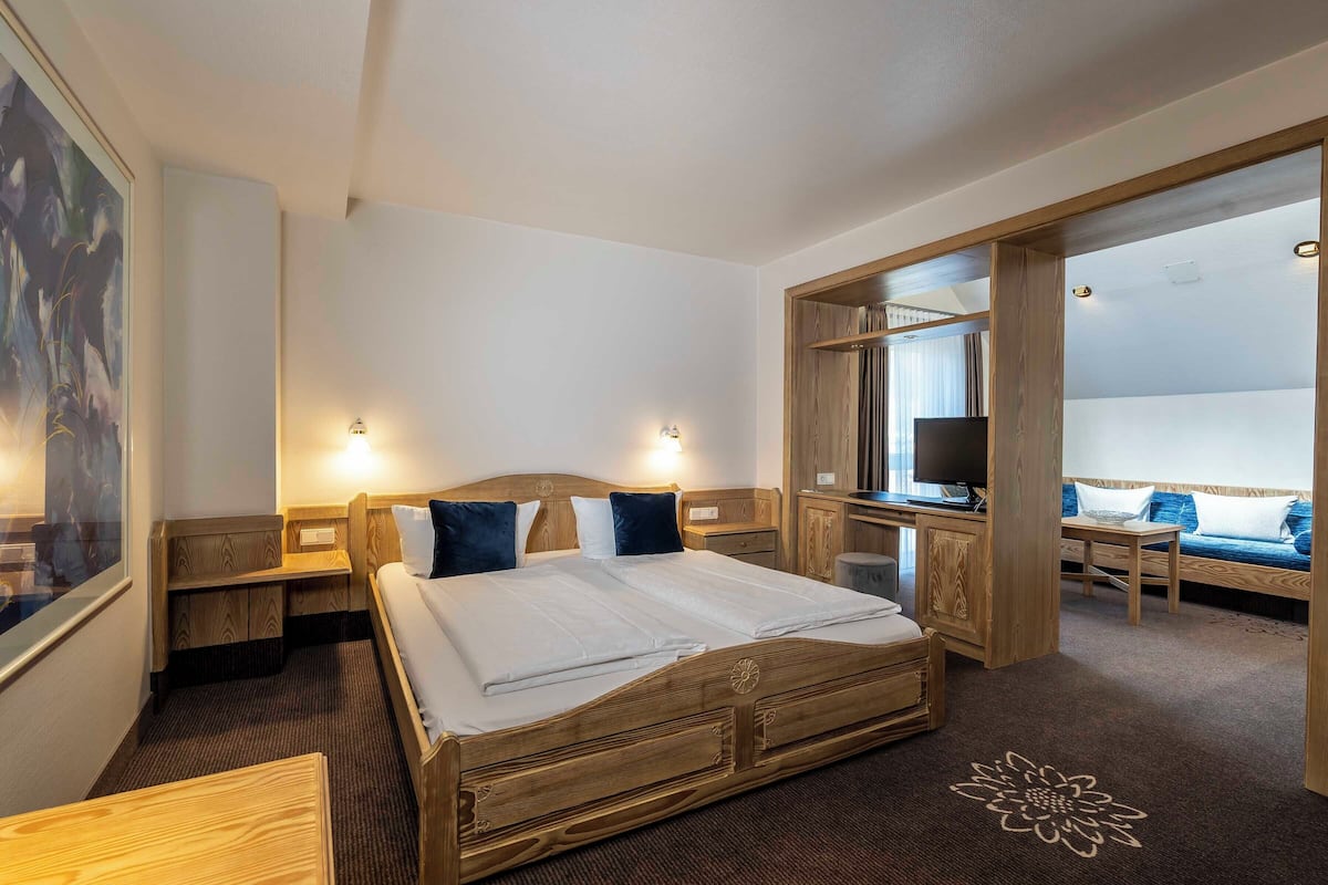 Ein Hotelzimmer mit einem hölzernen Bett, Nachttischen, einem Schreibtisch und einem Fernseher.