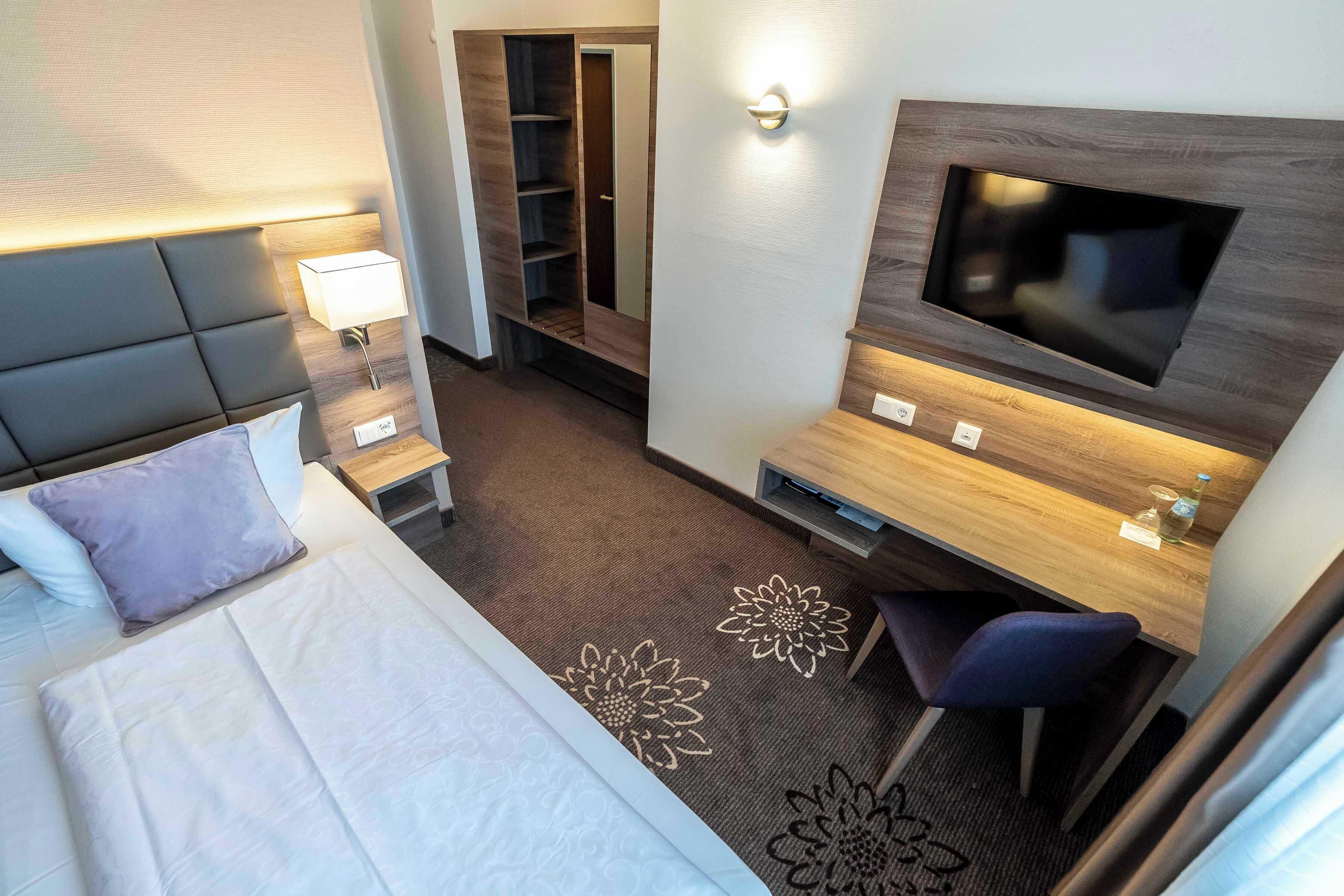 A hotel room with a bed, a desk, a TV, a wardrobe, and a bathroom.