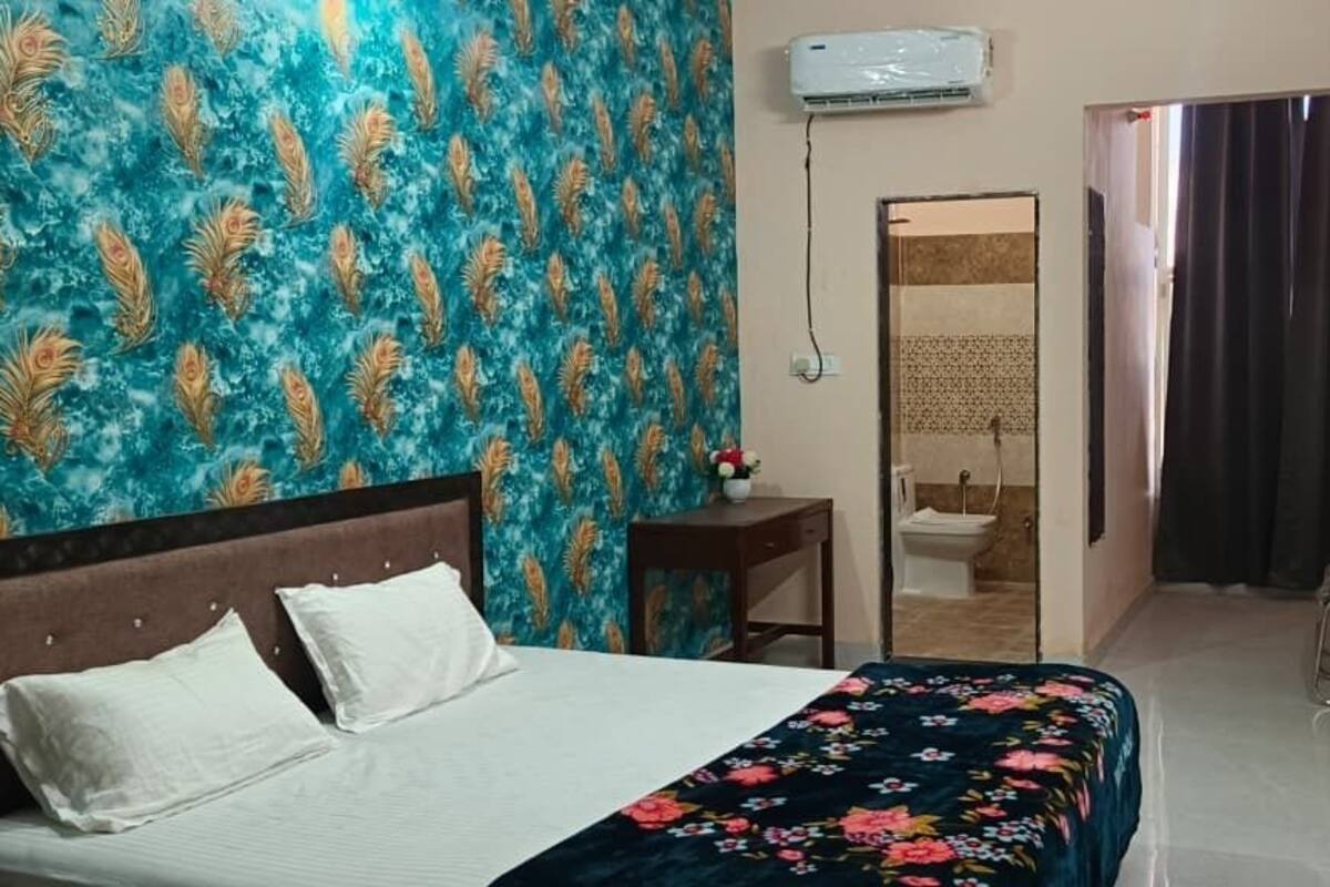 A hotel room with a bed, a small table with a vase, a shower area, and a TV mounted on the wall.