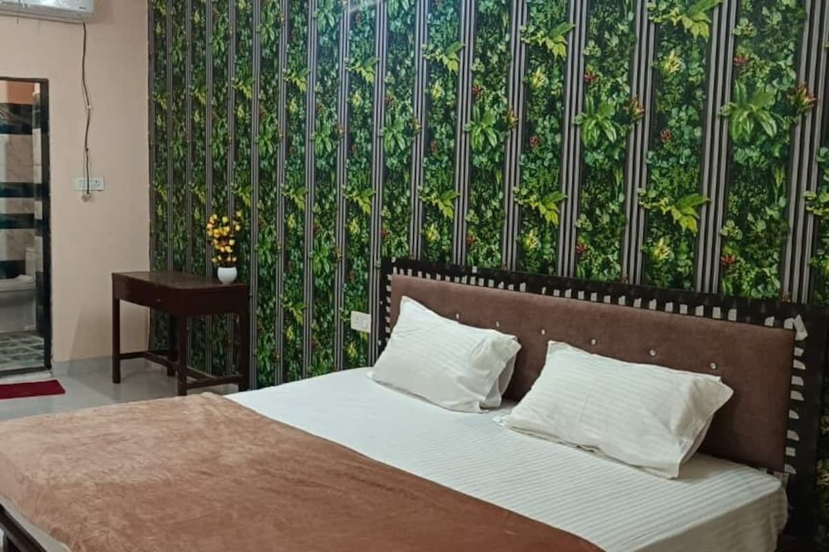 A hotel room with a bed, a small table, a chair, a bathroom with a shower, and a curtain.