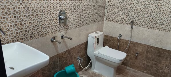 Une salle de bain avec un lavabo, des toilettes et une douche, le tout de couleur blanche. Les murs sont ornés d’un motif décoratif.