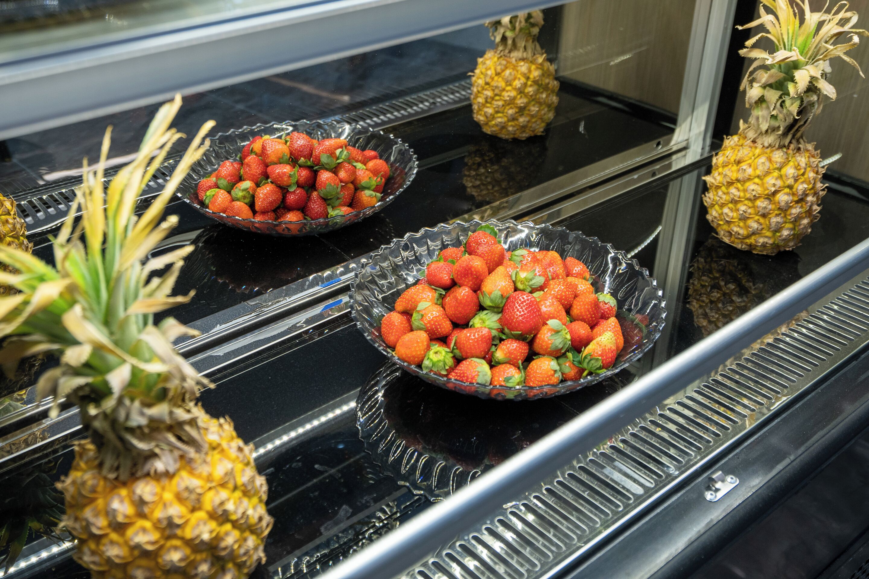Une présentation de fraises et d’ananas frais sur une surface noire réfléchissante.