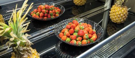Une présentation de fraises et d’ananas frais sur une surface noire réfléchissante.