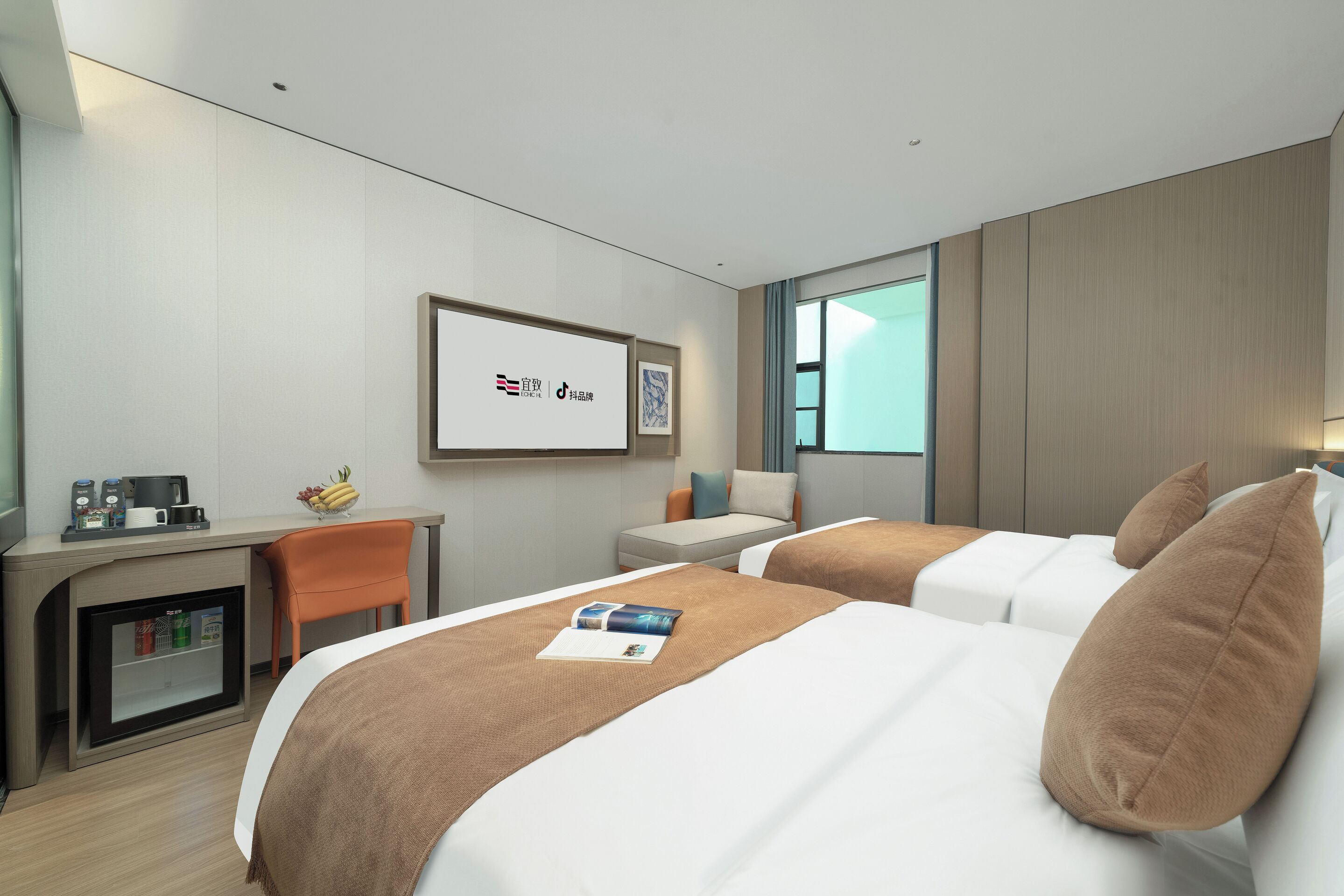 Habitación de hotel con dos camas, un escritorio, una silla, una mesita con cafetera y fruta, y un cuadro en la pared.